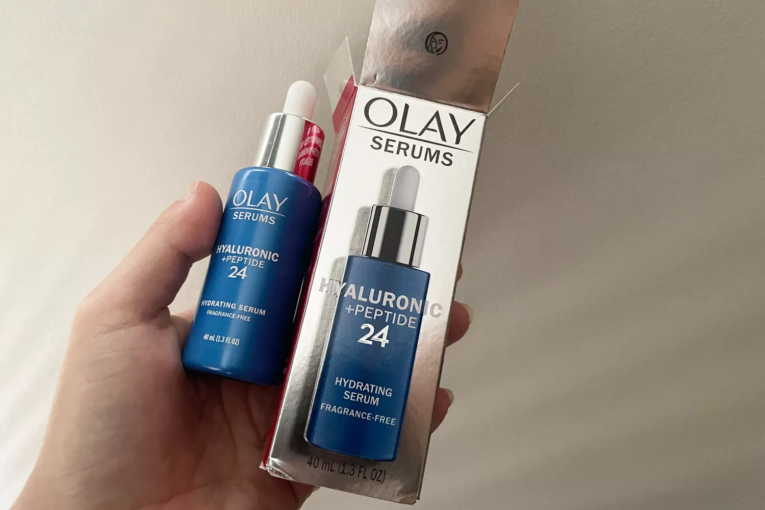 A person holds a bottle of OLAY Hyaluronic + Peptide 24 Serum and the box